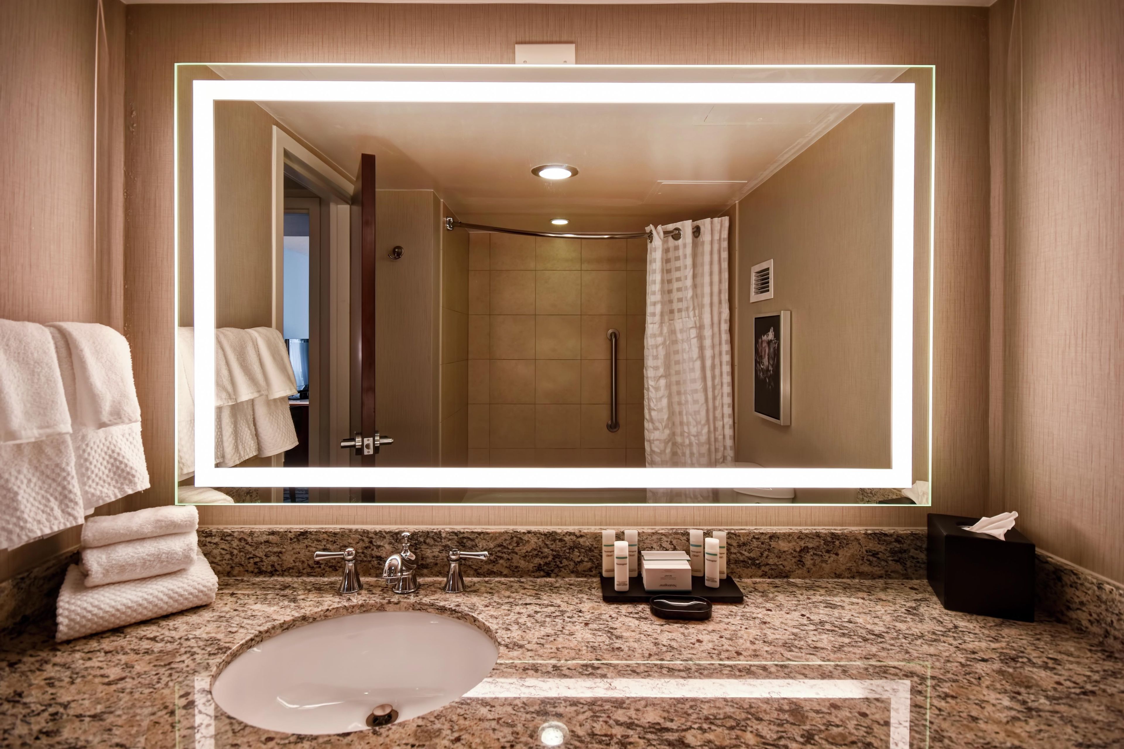 A bathroom with a large mirror, a sink, and a shower area.