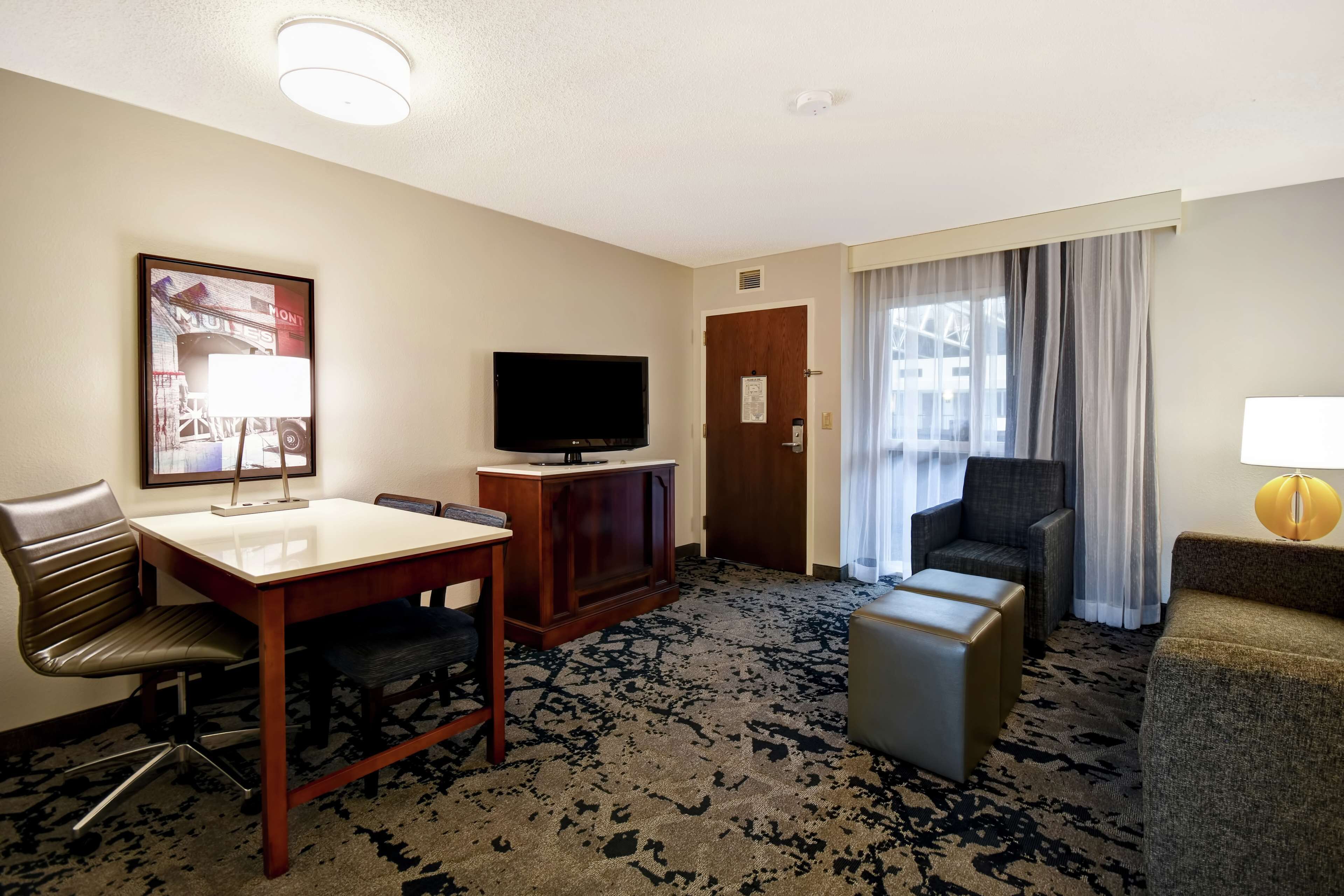 A hotel room with a flat-screen TV, a wooden desk, a comfortable armchair, a sofa, and a small ottoman.