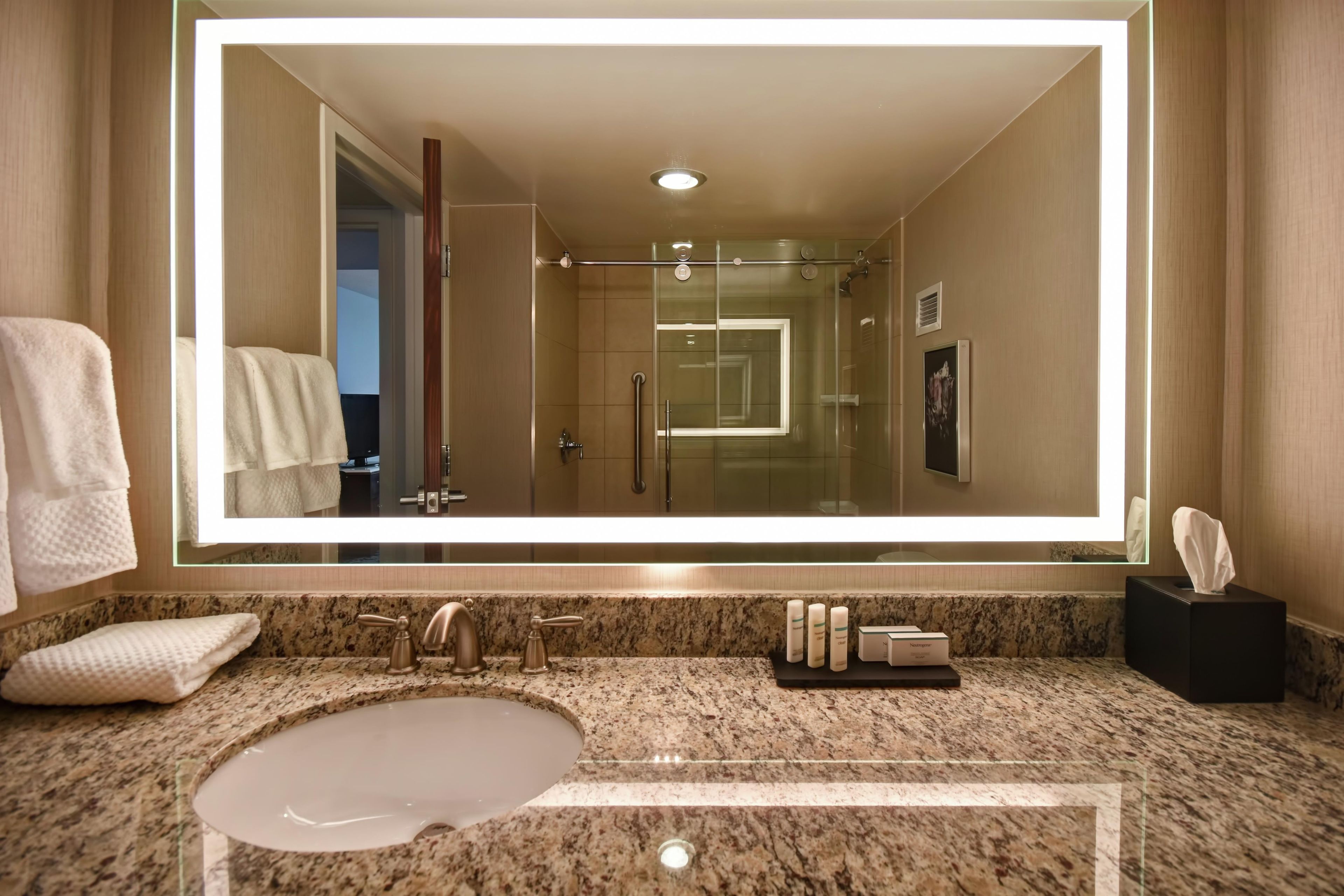 A hotel bathroom with a large mirror, a sink, and a glass-enclosed shower.