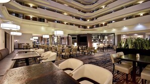 Un'ampia hall d'hotel con diverse aree ristorazione, posti a sedere confortevoli e un design moderno.