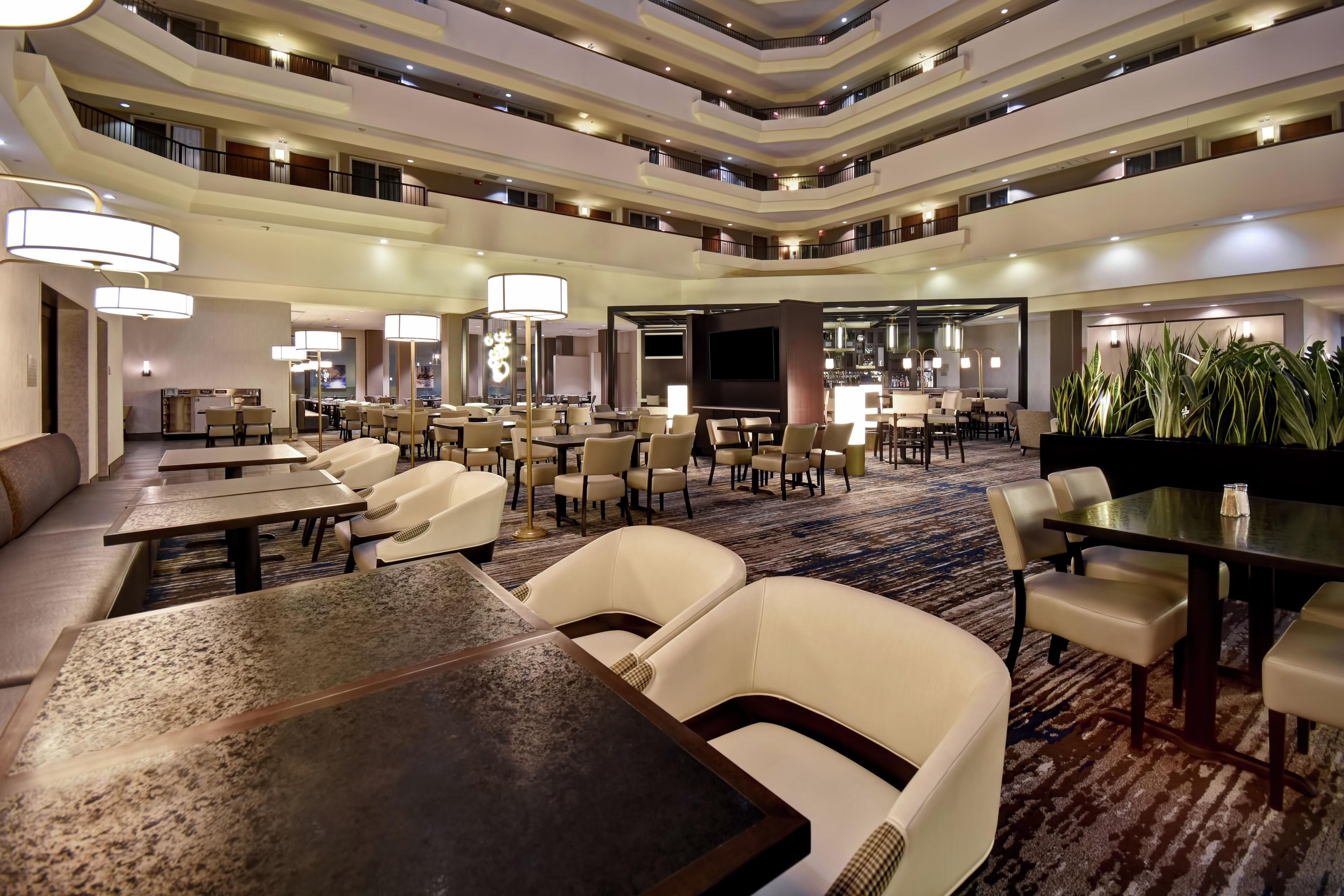 Vestíbulo de hotel con varios niveles, zonas de comedor, asientos y un bar.