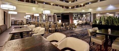Vestíbulo de hotel con varios niveles, zonas de comedor, asientos y un bar.