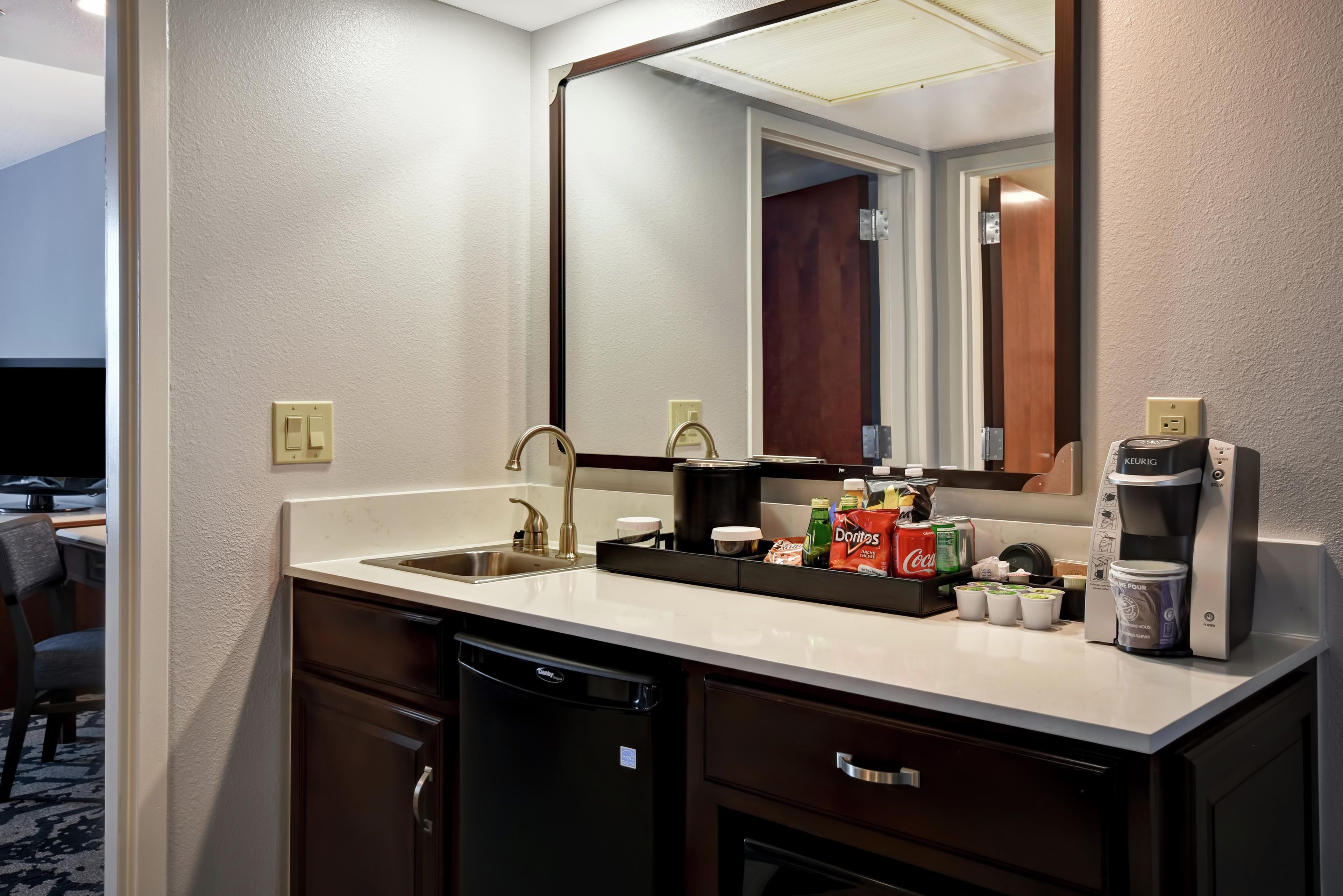 A hotel bathroom with a sink, mirror, and a coffee maker.