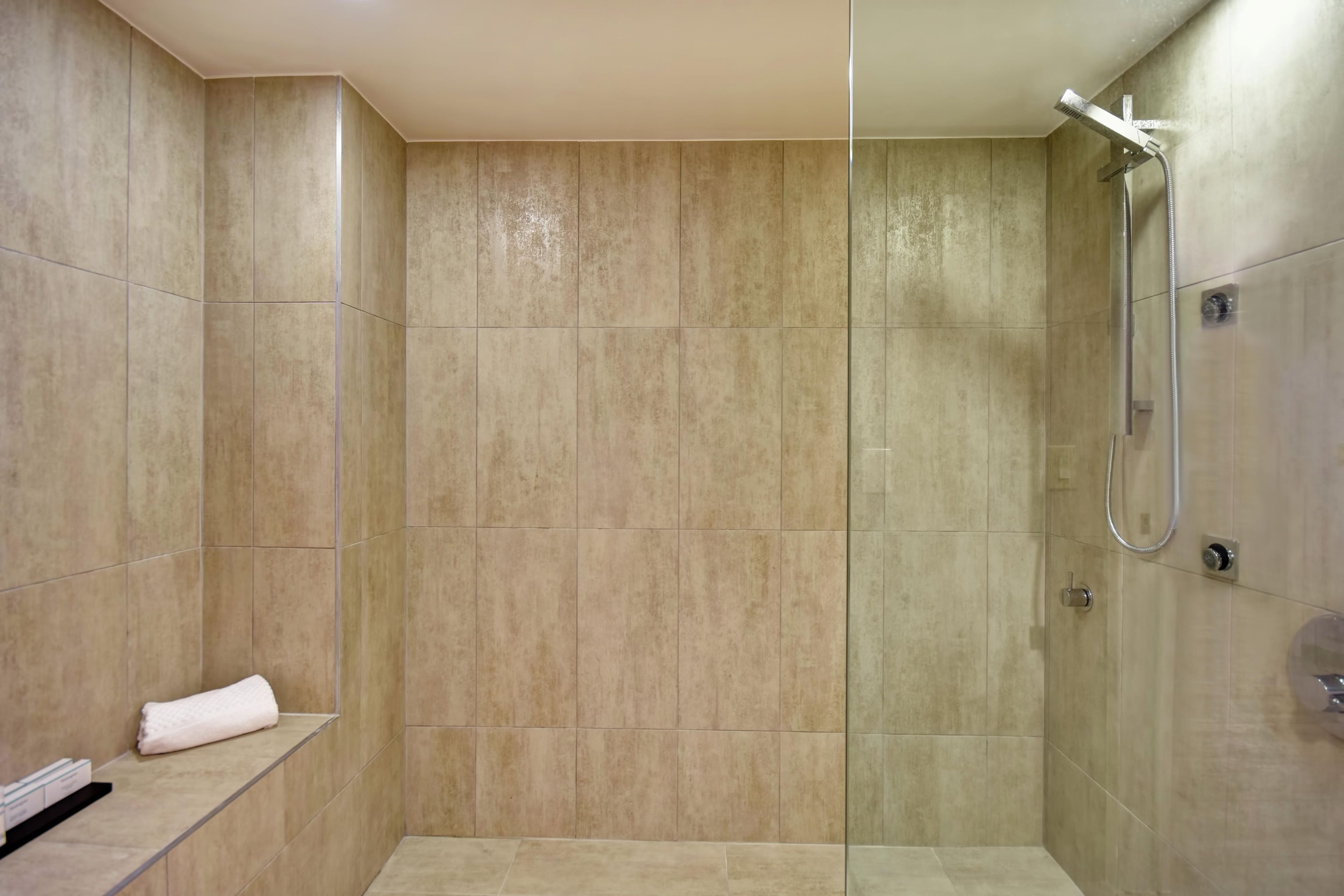 A walk-in shower with beige tiles, a glass partition, and a towel on a shelf.