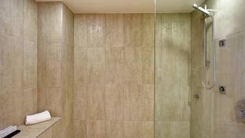 A walk-in shower with beige tiles, a glass partition, and a towel on a shelf.