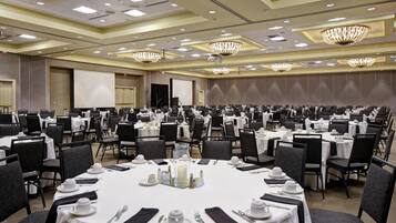 A large conference room with multiple round tables, each set with white tablecloths, chairs, and silverware.