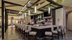 Un'area bar moderna con un lungo bancone, diversi sgabelli e lampade a sospensione.