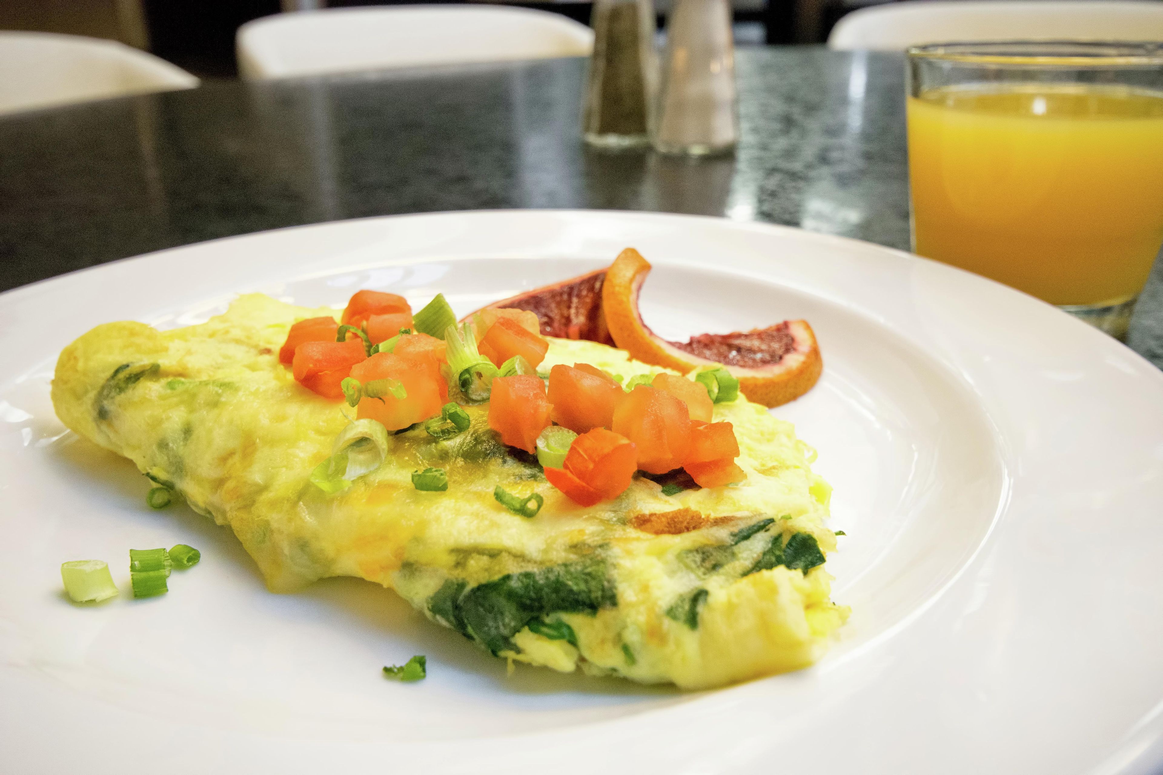 A plate with an omelette, tomatoes, and a slice of blood orange on a white plate.