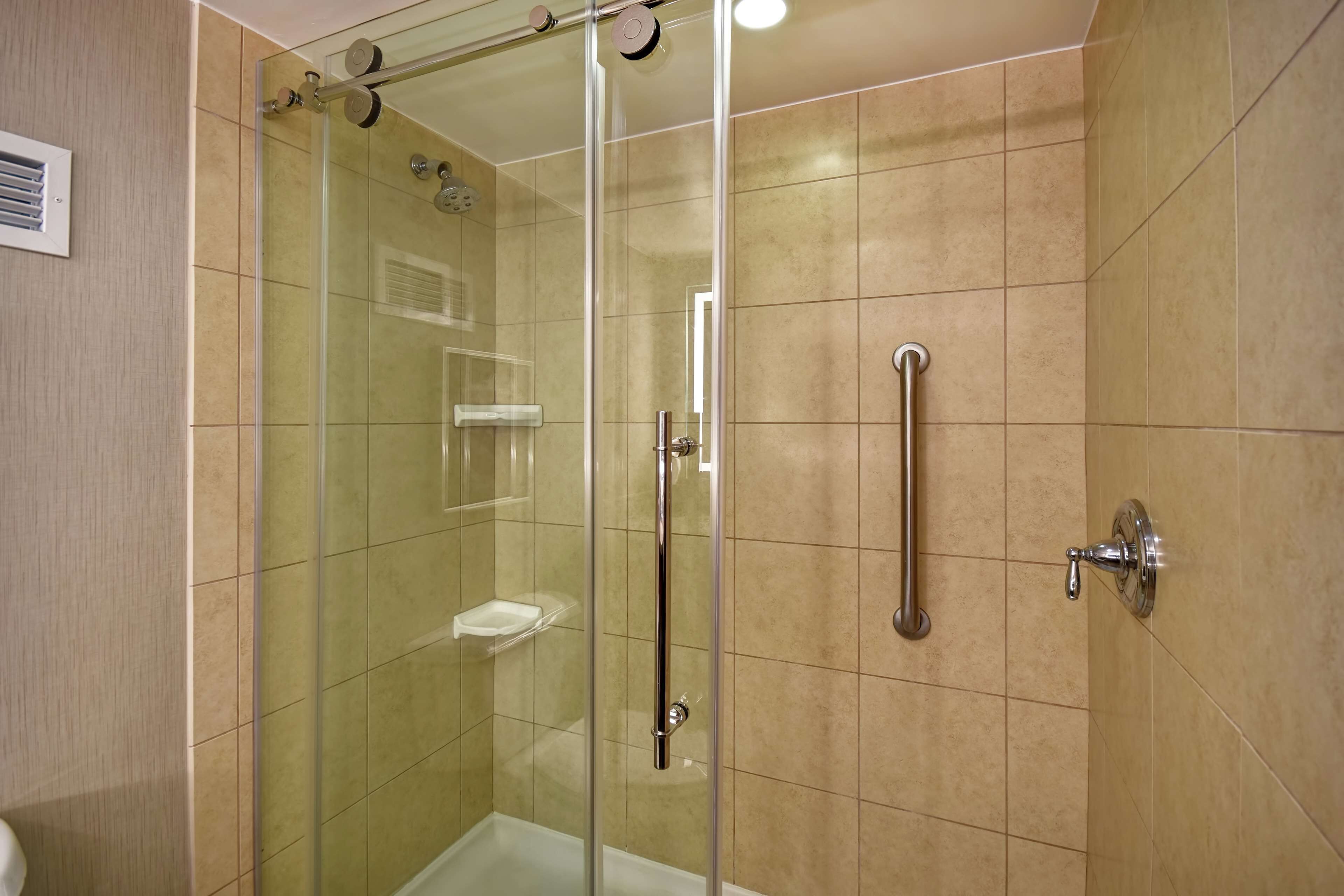 A glass-enclosed shower stall with a handheld showerhead, a handheld shower control, and a wall-mounted faucet.