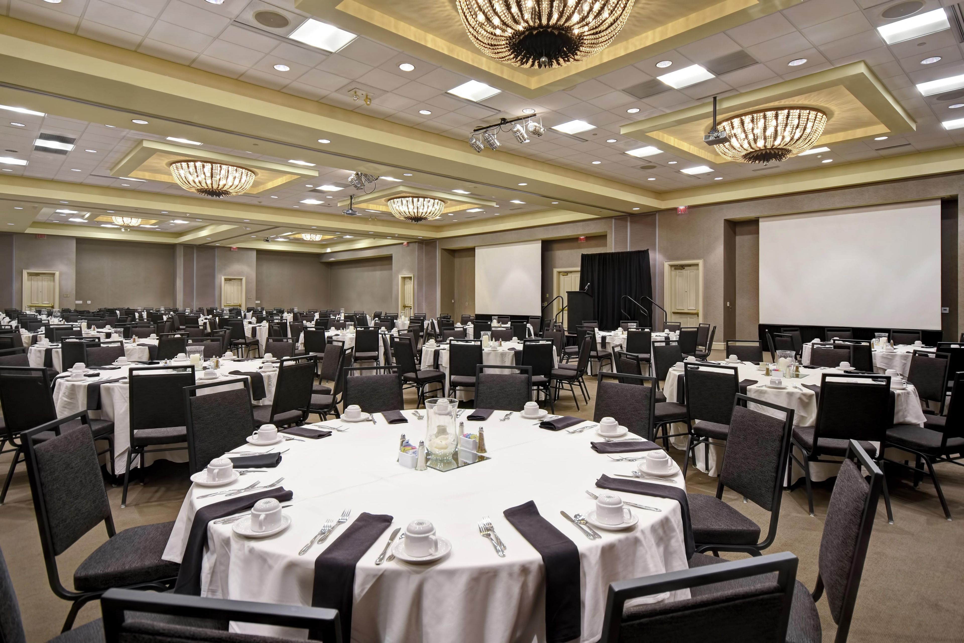 A large conference room with round tables, black chairs, and chandeliers.