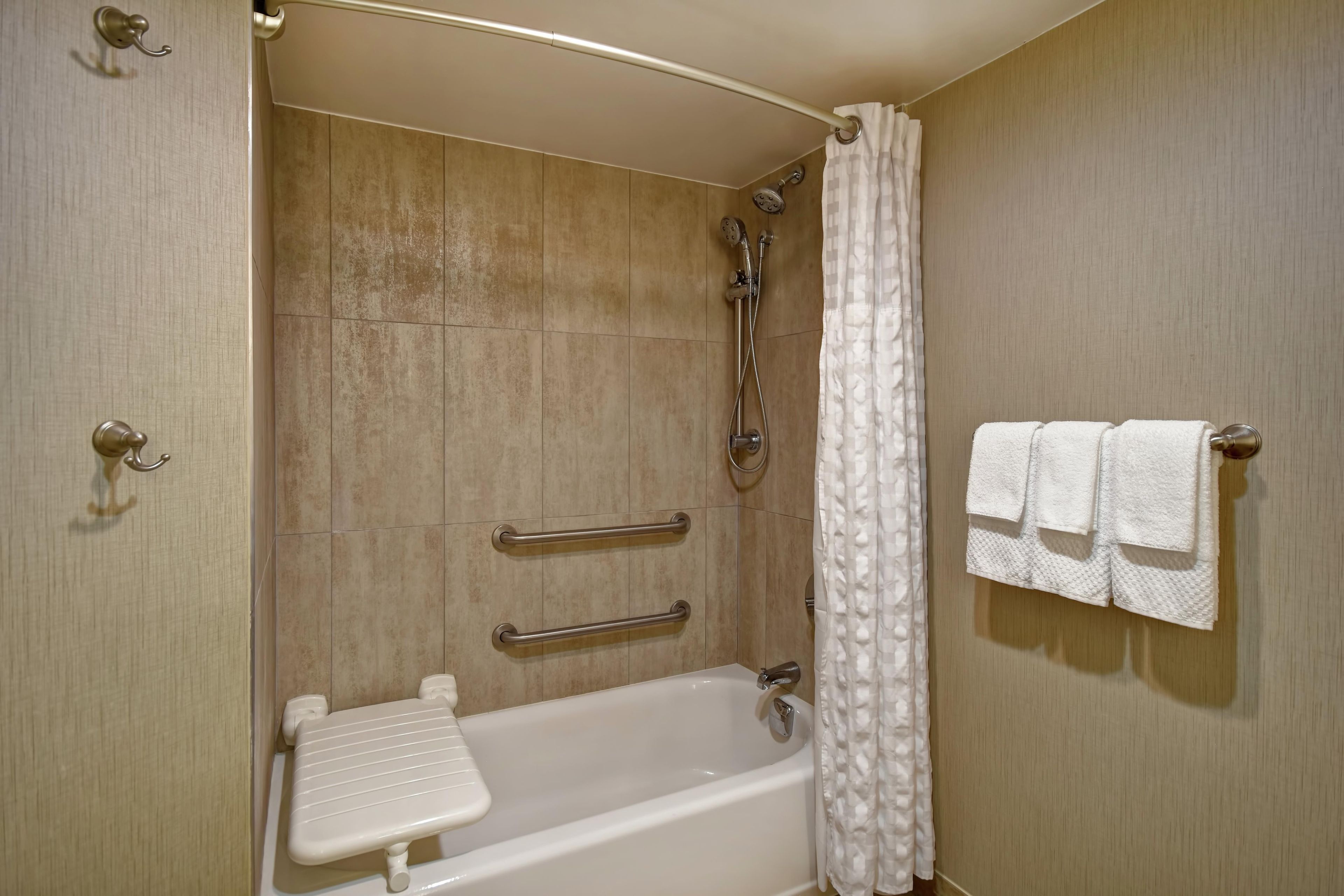 A bathroom with a bathtub, shower, and handrails.