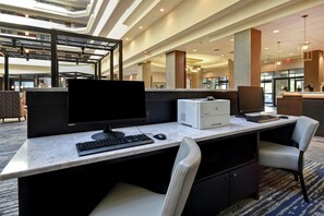 A hotel lobby with a reception desk, a large flat-screen monitor, a desktop computer, and a seating area with a chair. - Embassy Suites by Hilton Montgomery Hotel & Conference Ctr (Montgomery)