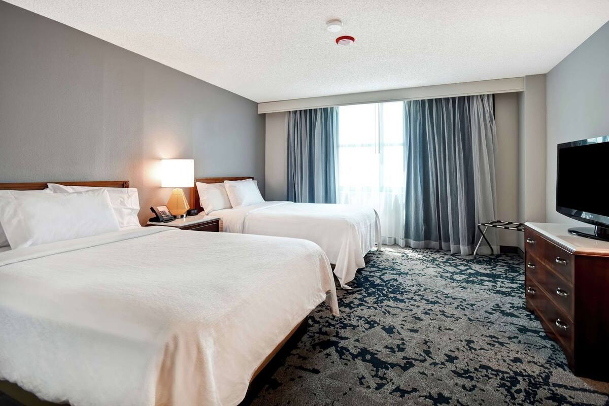 A hotel room with two beds, a television, a desk, and a window with curtains.