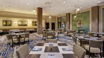Une salle à manger d’hôtel avec plusieurs tables et chaises, une moquette à motifs et des œuvres d’art accrochées aux murs.