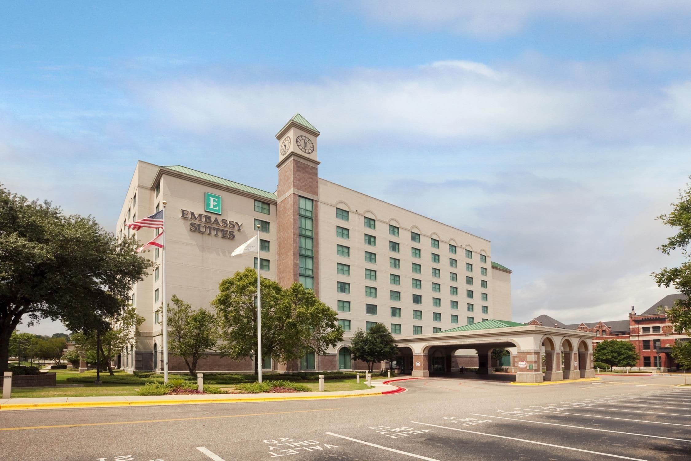 A large hotel building with a prominent clock tower, multiple floors, and a flagpole with flags.