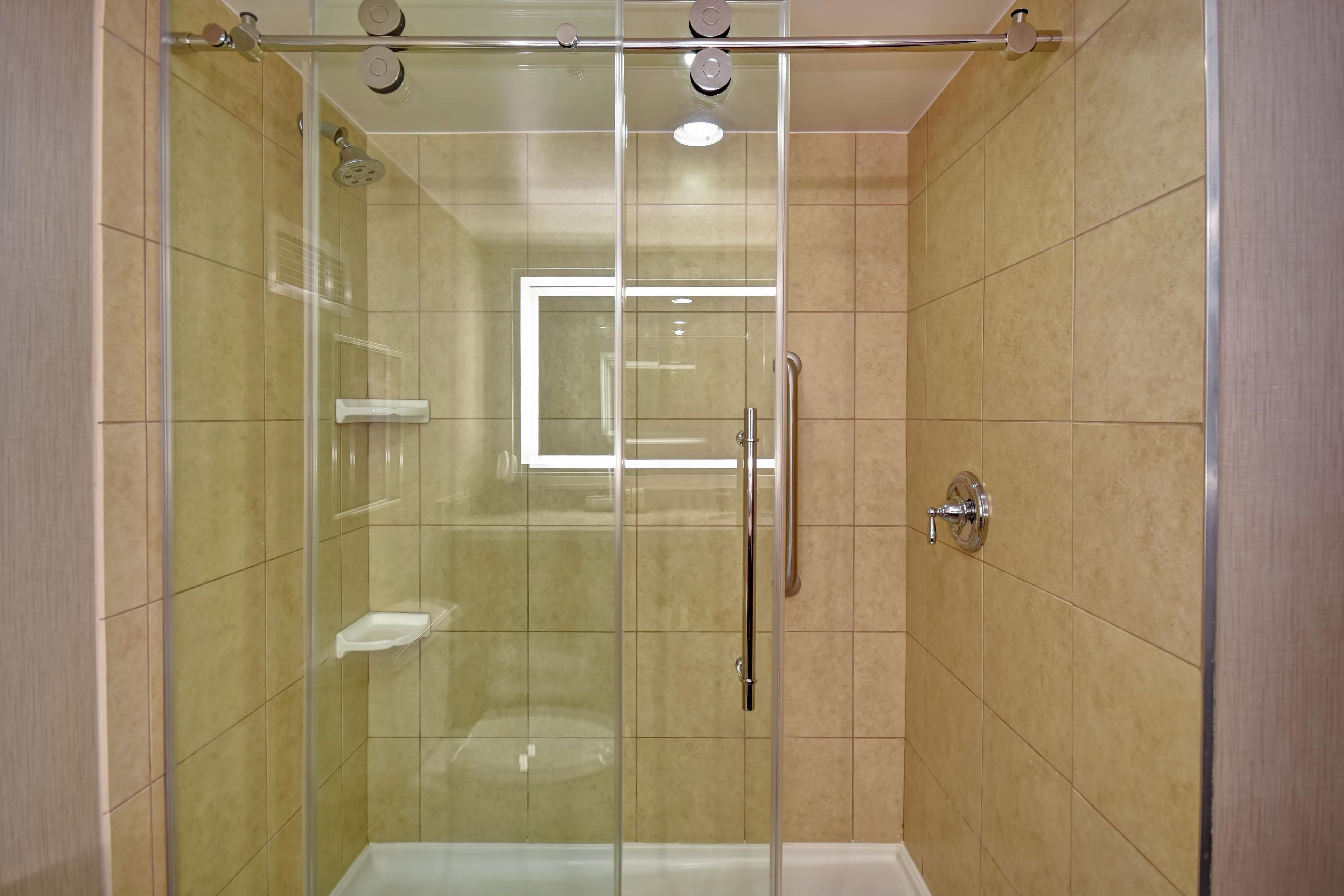 A glass-enclosed shower stall with a handheld showerhead, a handheld showerhead, and a handheld showerhead.