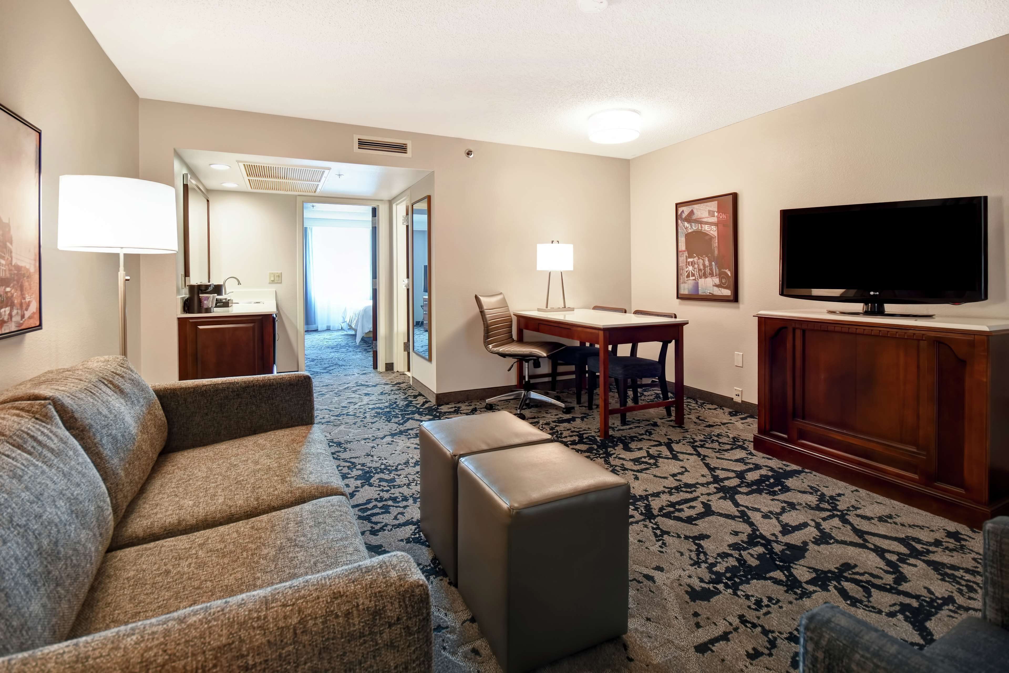 Ein Hotelzimmer mit Sofa, Hocker, Esstisch, Stühlen, Fernseher und Lampe.
