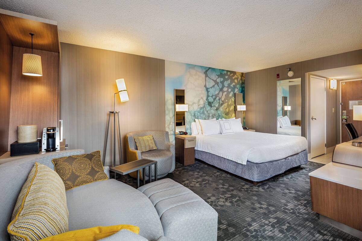 A hotel room with a bed, a sofa, a chair, a desk, and a mirror.