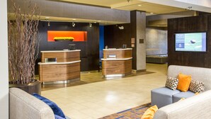 A hotel lobby with a reception desk, seating area, and a TV screen displaying a sports game. - Courtyard by Marriott Riverside UCR/Moreno Valley Area (Riverside)