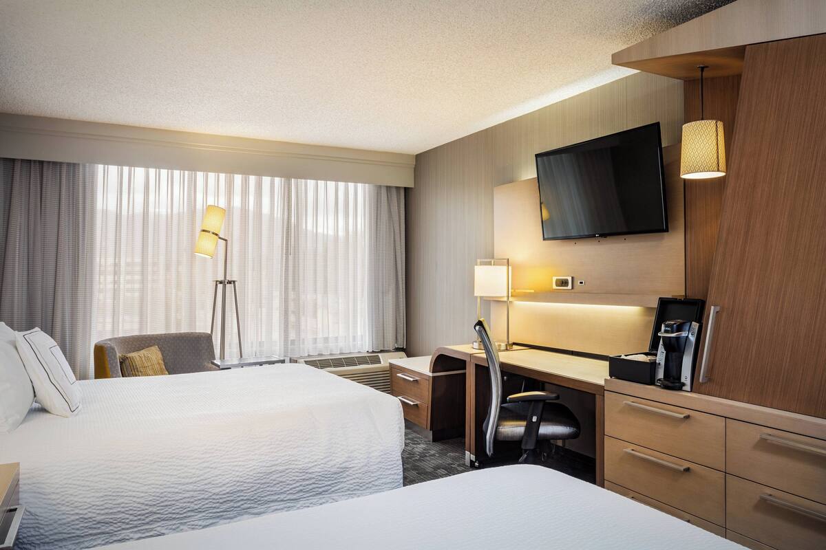 A hotel room with two beds, a desk, a chair, a television, and a window with curtains.