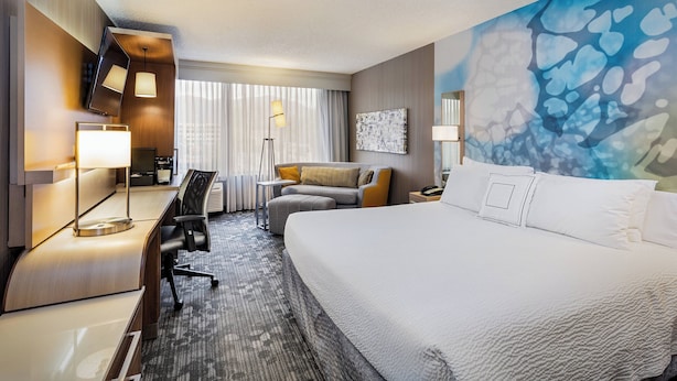 A hotel room with a large bed, a desk with a lamp, a sofa, and a painting on the wall. - Courtyard by Marriott Riverside UCR/Moreno Valley Area (Riverside)