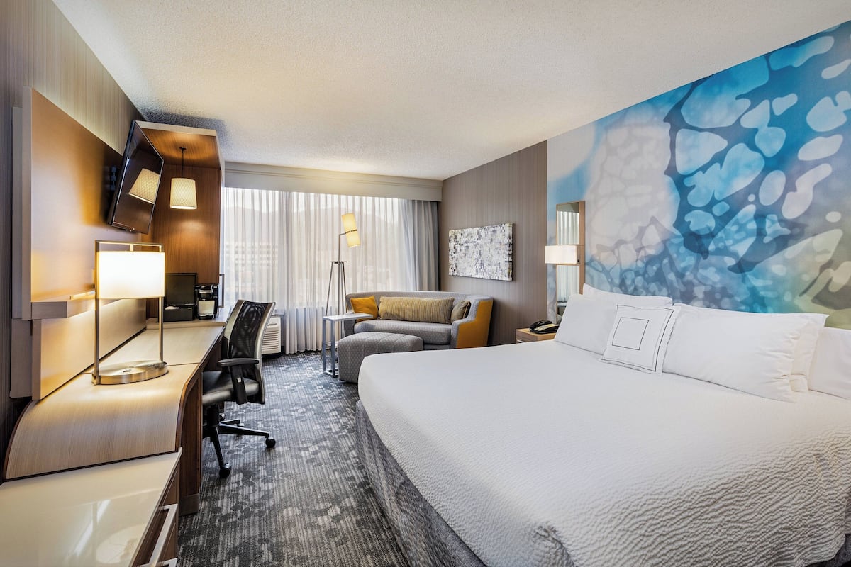 A hotel room with a large bed, a desk with a lamp, a sofa, and a painting on the wall.