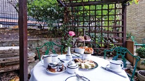 A garden setting with a table set for a tea party, featuring a variety of sandwiches, pastries, and a rose. - Grange Blooms Hotel (London)