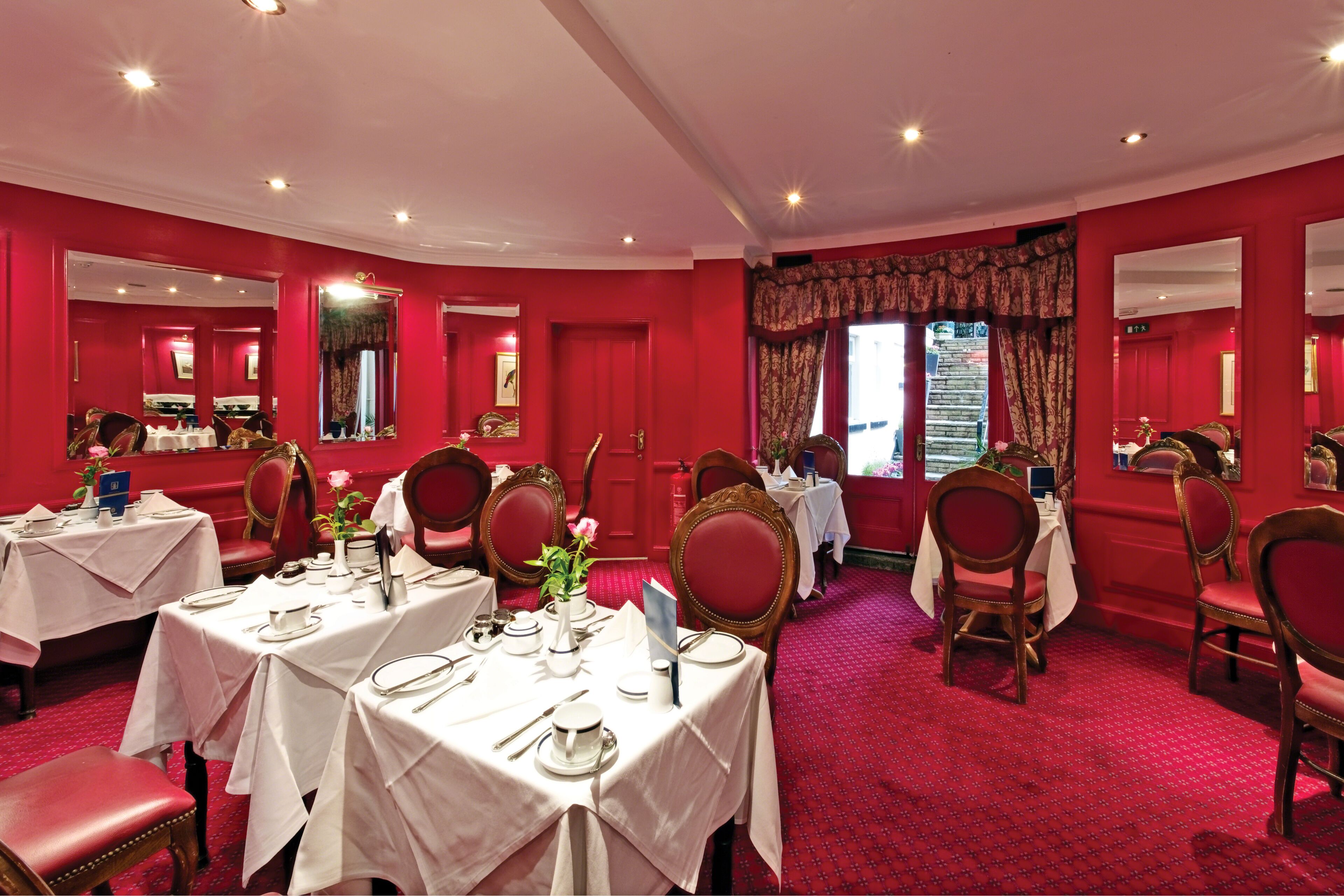 A formal dining room with red walls, white tables, and red chairs.
