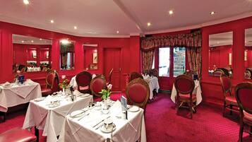 A formal dining room with red walls, white tables, and red chairs.