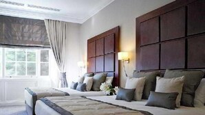 A hotel room with two beds, a large window with curtains, and a dark wooden headboard. - Grange Blooms Hotel (London)