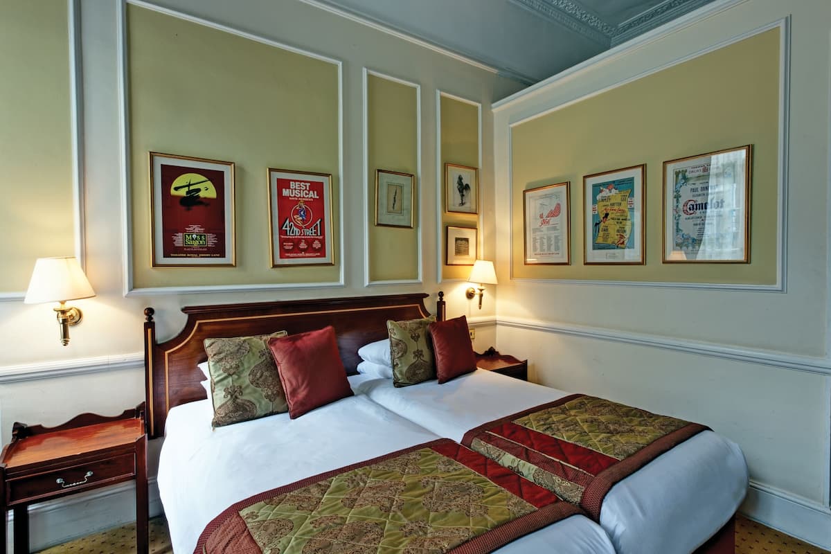 Ein Hotelzimmer mit einem großen Bett, zwei Nachttischen und Wandlampen. An den Wänden befinden sich gerahmte Poster.