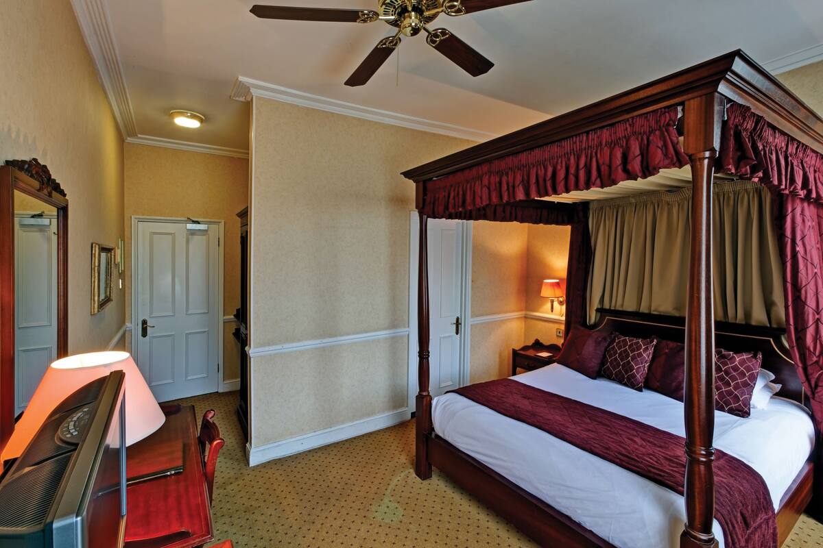 Ein Hotelzimmer mit einem Himmelsbett, einem Schreibtisch mit Lampe und einem Deckenventilator.