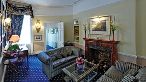 A traditional living room with striped sofas, a glass coffee table, a fireplace, and a blue patterned carpet. - Grange Blooms Hotel (London)