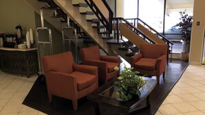 A lobby with a staircase, red patterned chairs, a glass coffee table, and a plant.