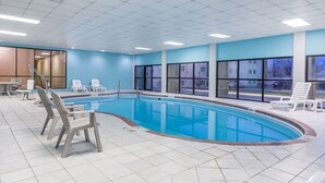 An indoor swimming pool with clear blue water, surrounded by white chairs and a tiled floor.