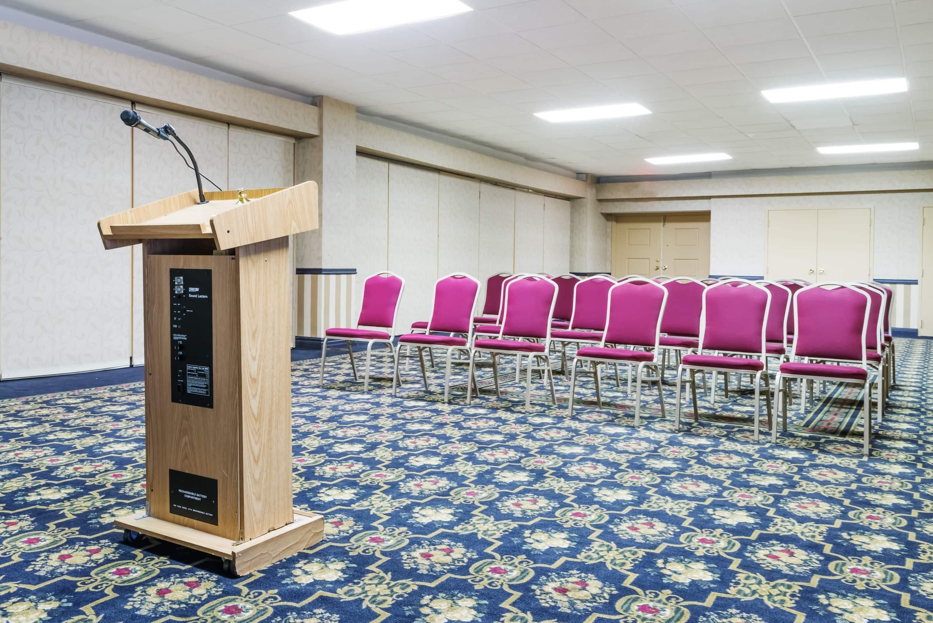 A room with a wooden podium, pink chairs, and a patterned carpet.