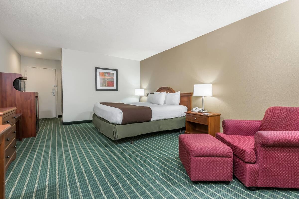 Une chambre d’hôtel avec un lit, un bureau, une chaise, une table de chevet et une lampe.