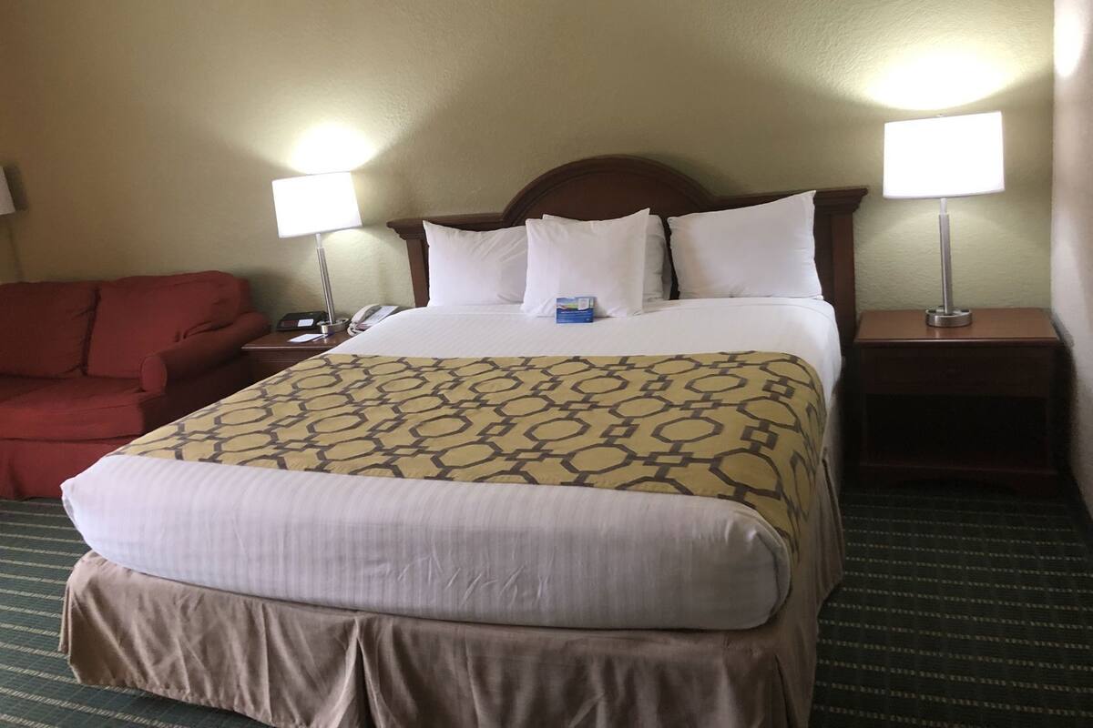 Une chambre d’hôtel avec un lit, deux lampes de chevet, un fauteuil rouge et une table de chevet avec un téléphone.