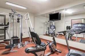 A gym with exercise equipment, a television, and a mirror. - Baymont by Wyndham Kokomo (Kokomo)