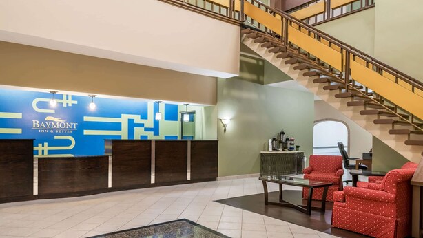 A hotel lobby with a reception desk, a staircase, and seating area.
