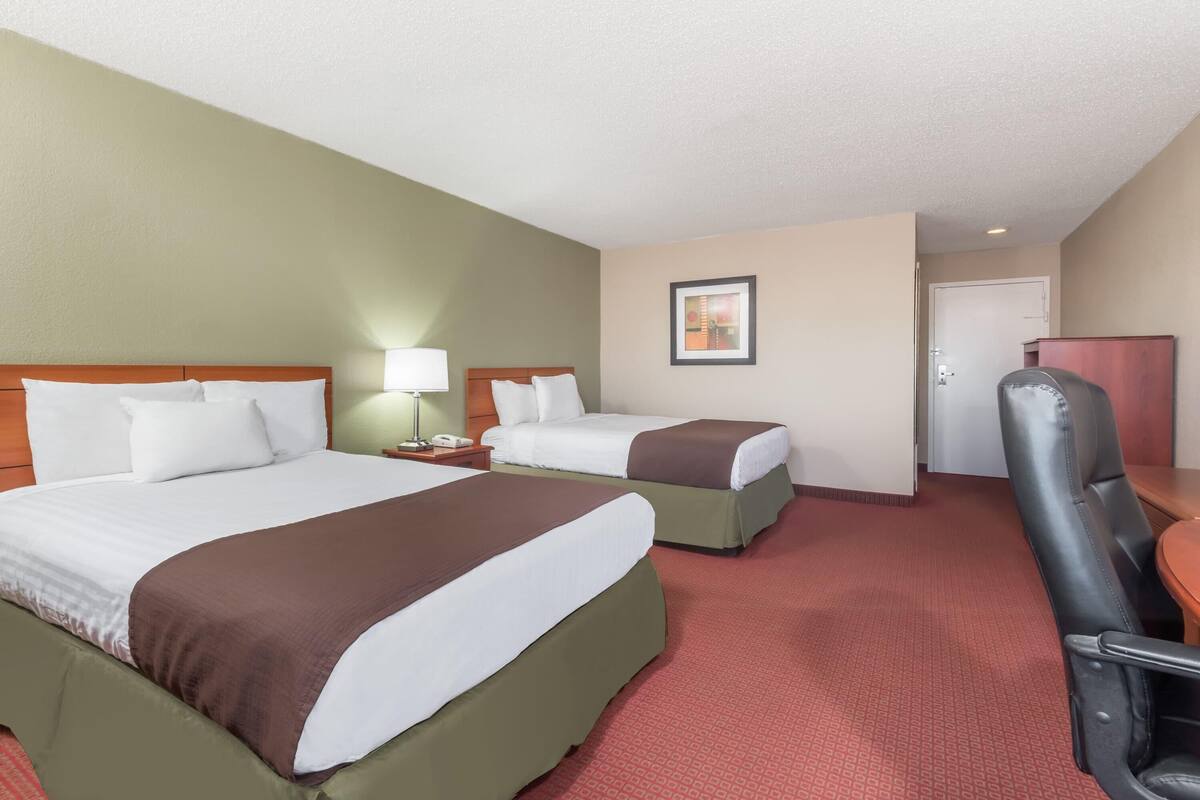 Une chambre d’hôtel avec deux lits, un bureau, une chaise et une porte.