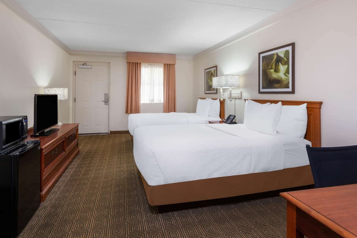 A hotel room with a large bed, a desk with a television, a lamp, and a painting on the wall.