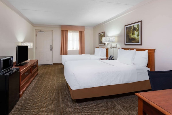 A hotel room with a large bed, a desk with a television, a lamp, and a painting on the wall.
