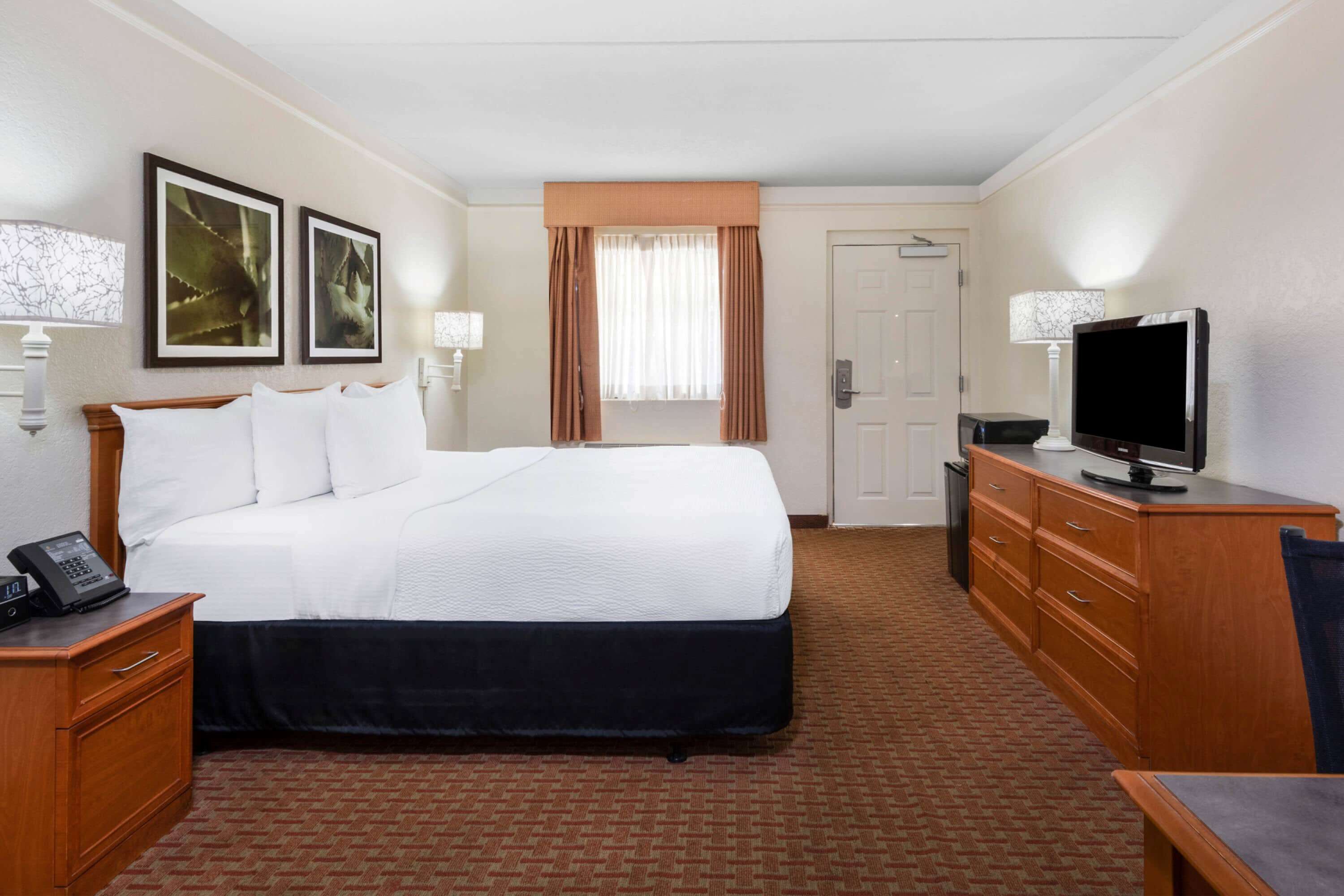 A hotel room with a large bed, a desk with a telephone, a television, and a wardrobe.