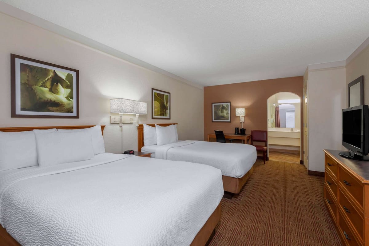 A hotel room with two beds, a desk, a chair, a television, and artwork on the walls.