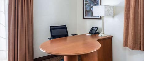 Habitación de hotel con un escritorio de madera, una silla de oficina negra, un teléfono, una lámpara y un cuadro en la pared.