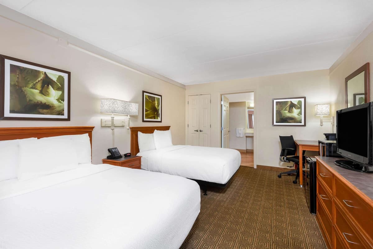 A hotel room with two beds, a desk, a television, and artwork on the walls.
