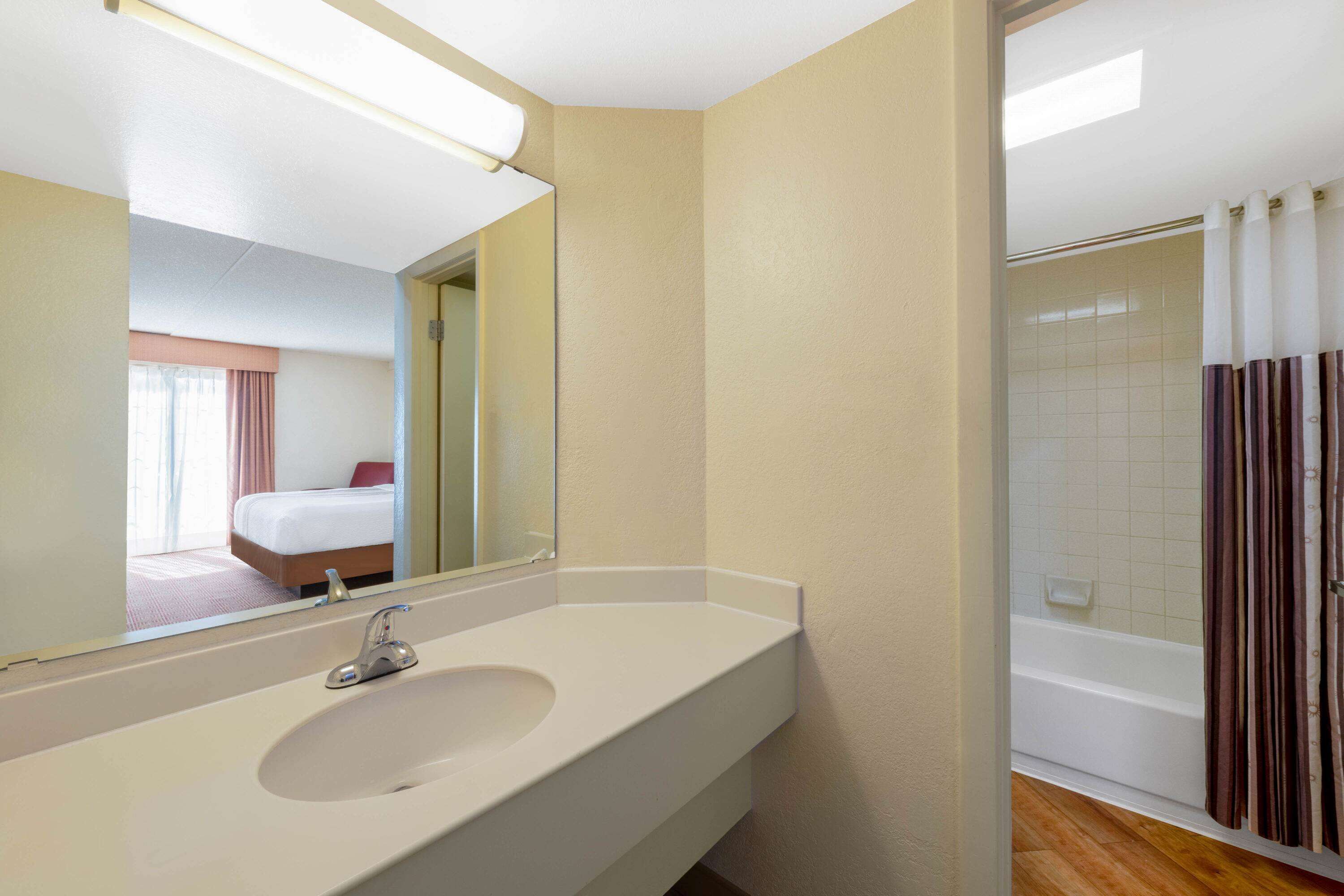 Une salle de bain d’hôtel avec un lavabo blanc, un miroir et une douche avec des rideaux à rayures.