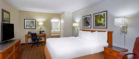 A hotel room with a bed, desk, chair, TV, and artwork on the walls.