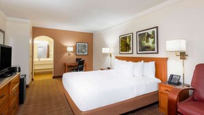 A hotel room with a large bed, a desk with a chair, a TV, a lamp, and artwork on the walls. - La Quinta East Deerfield Beach - Boca Raton (Deerfield Beach)